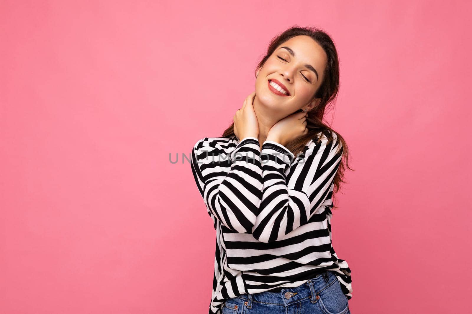 Photo portrait of young beautiful smiling hipster brunette woman in trendy pullover. Sexy carefree female person posing isolated near pink wall with empty space in studio. Positive model with natural makeup.