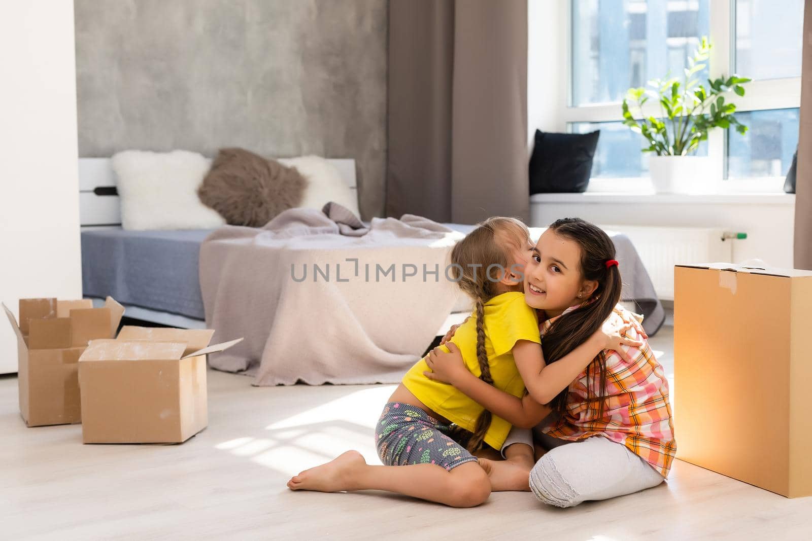 Happy family in living room. Preschool daughters sitting and help unpacking cardboard boxes belongings. Buy real estate, relocation at new modern house