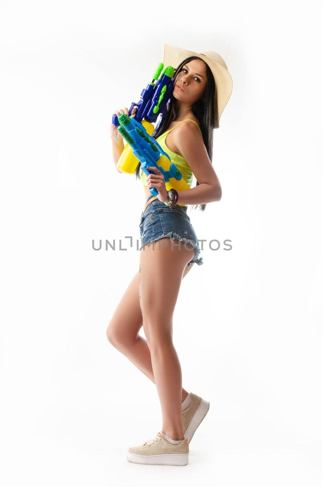 brunette girl with a water gun in summer clothes, slim and sexy isolated on a white background