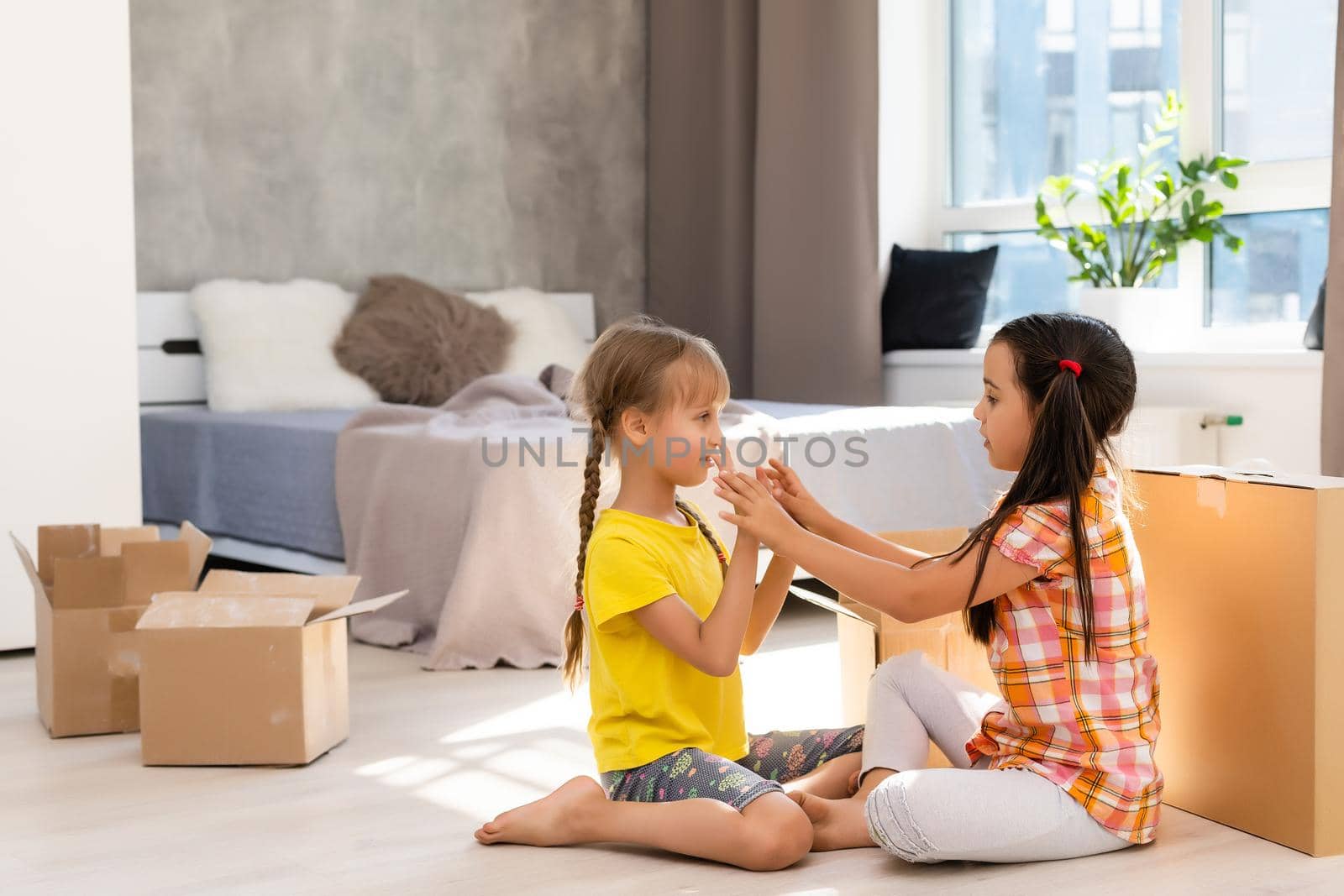 Happy family in living room. Preschool daughters sitting and help unpacking cardboard boxes belongings. Buy real estate, relocation at new modern house