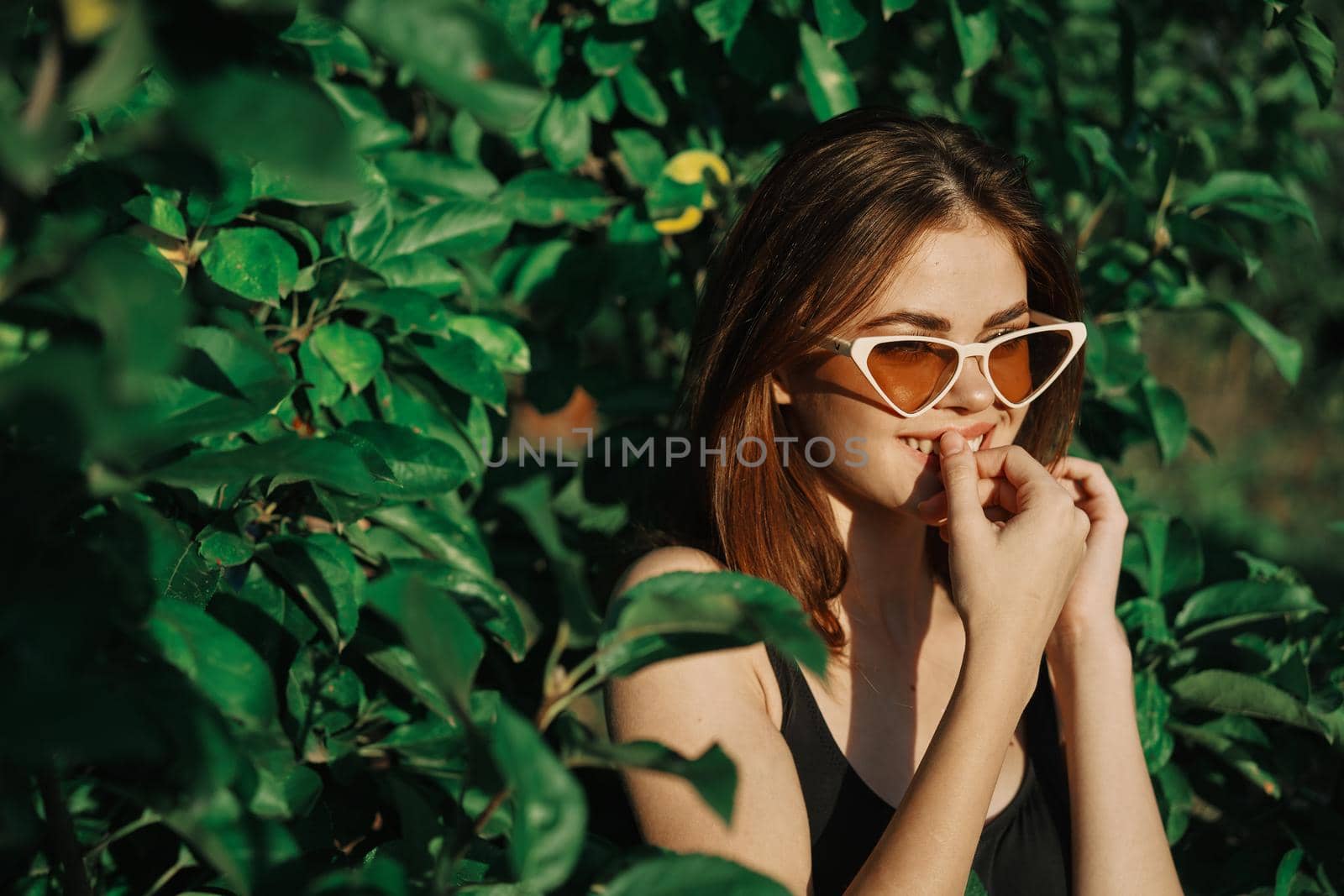 smiling woman wearing sunglasses green leaves nature fashion. High quality photo