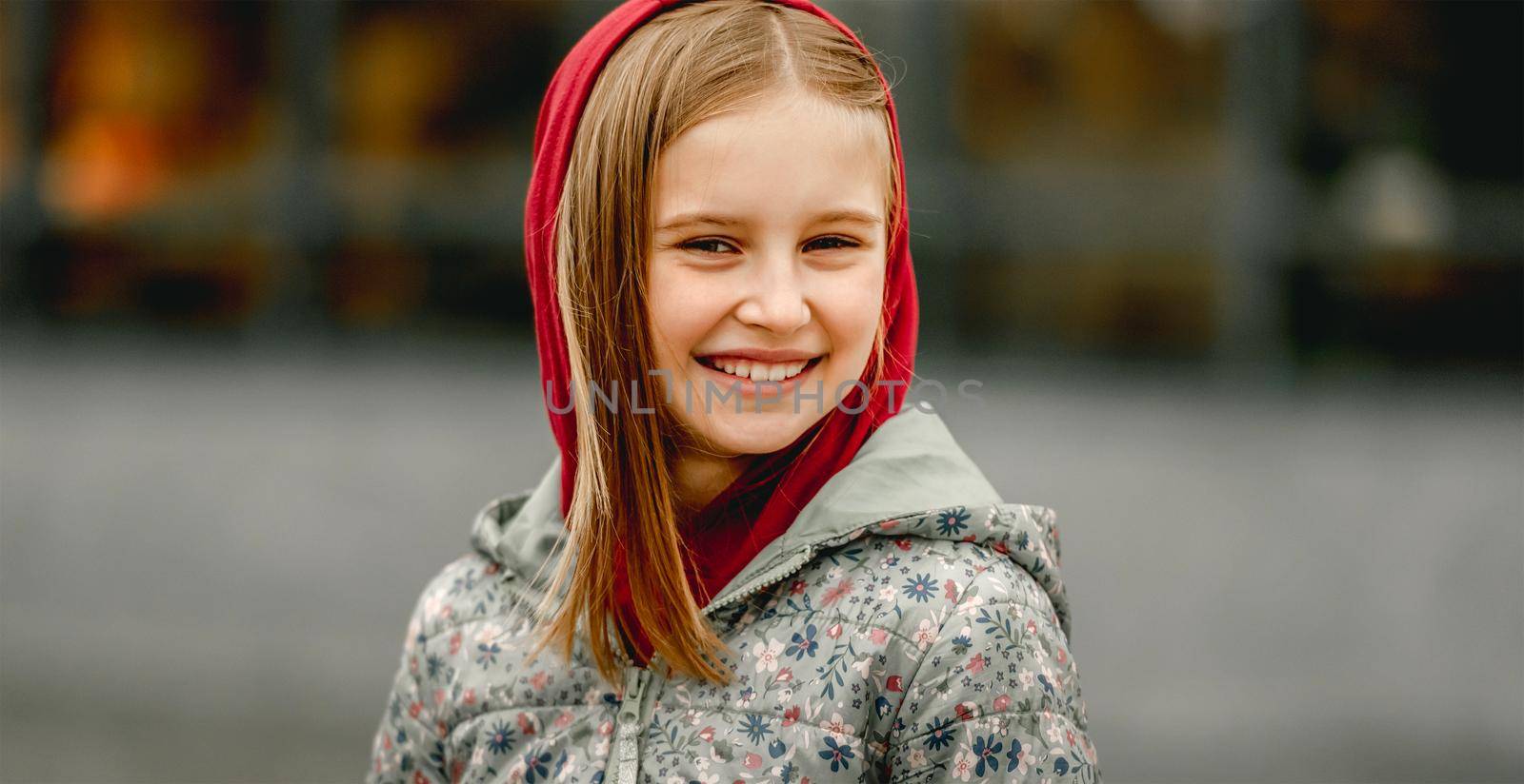 Preteen girl wearing hood and smiling at the street at autumn. Pretty female kid portrait outdoors in fall season