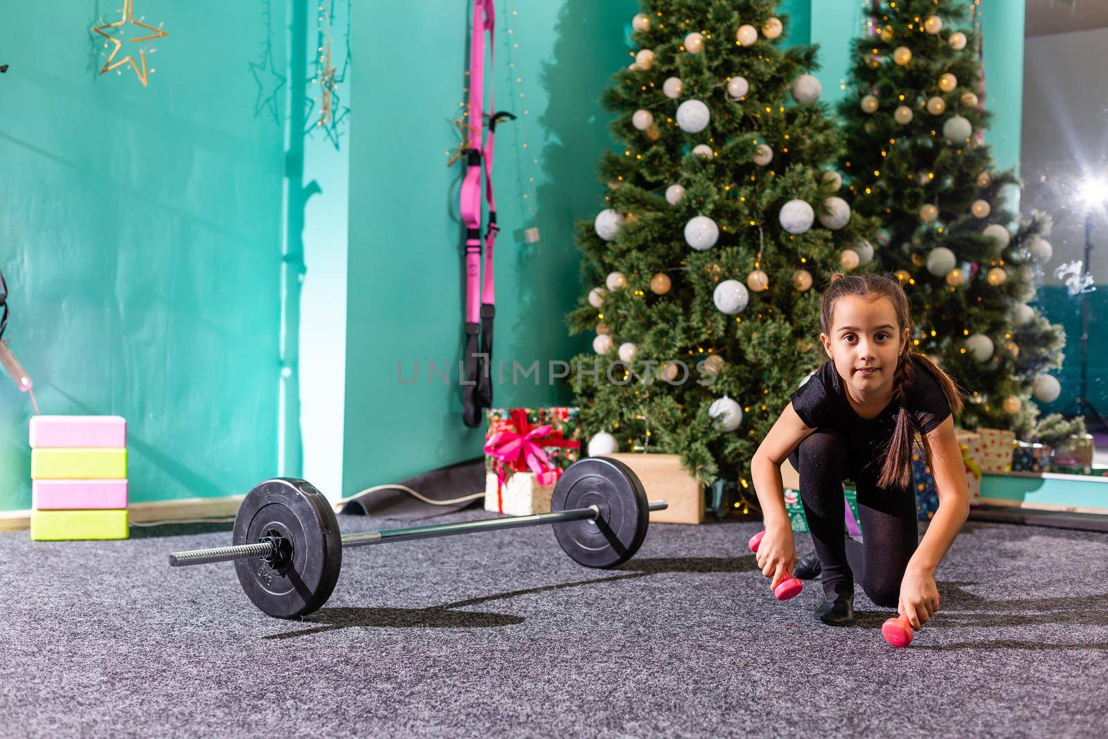 Merry Christmas and a happy new year. Little girl workout at home in christmas interior. Little dark-haired female model has exercises by Andelov13