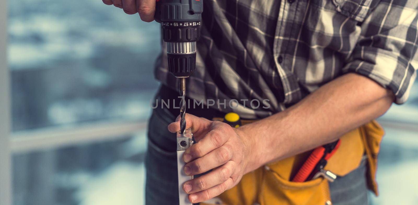 Man working making holes in board with drill during process of furniture manufacturing