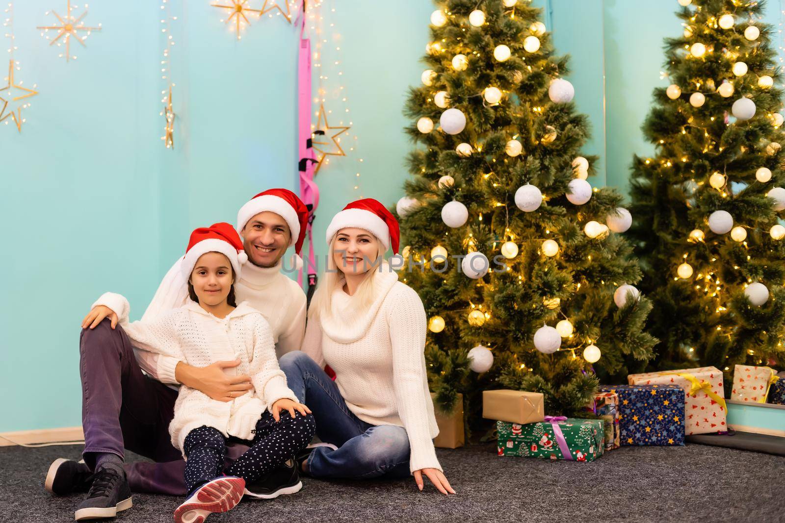 Christmas. Family. Happiness. dad, mom and daughter in Santa hats looking at camera and smiling on the floor at home by Andelov13