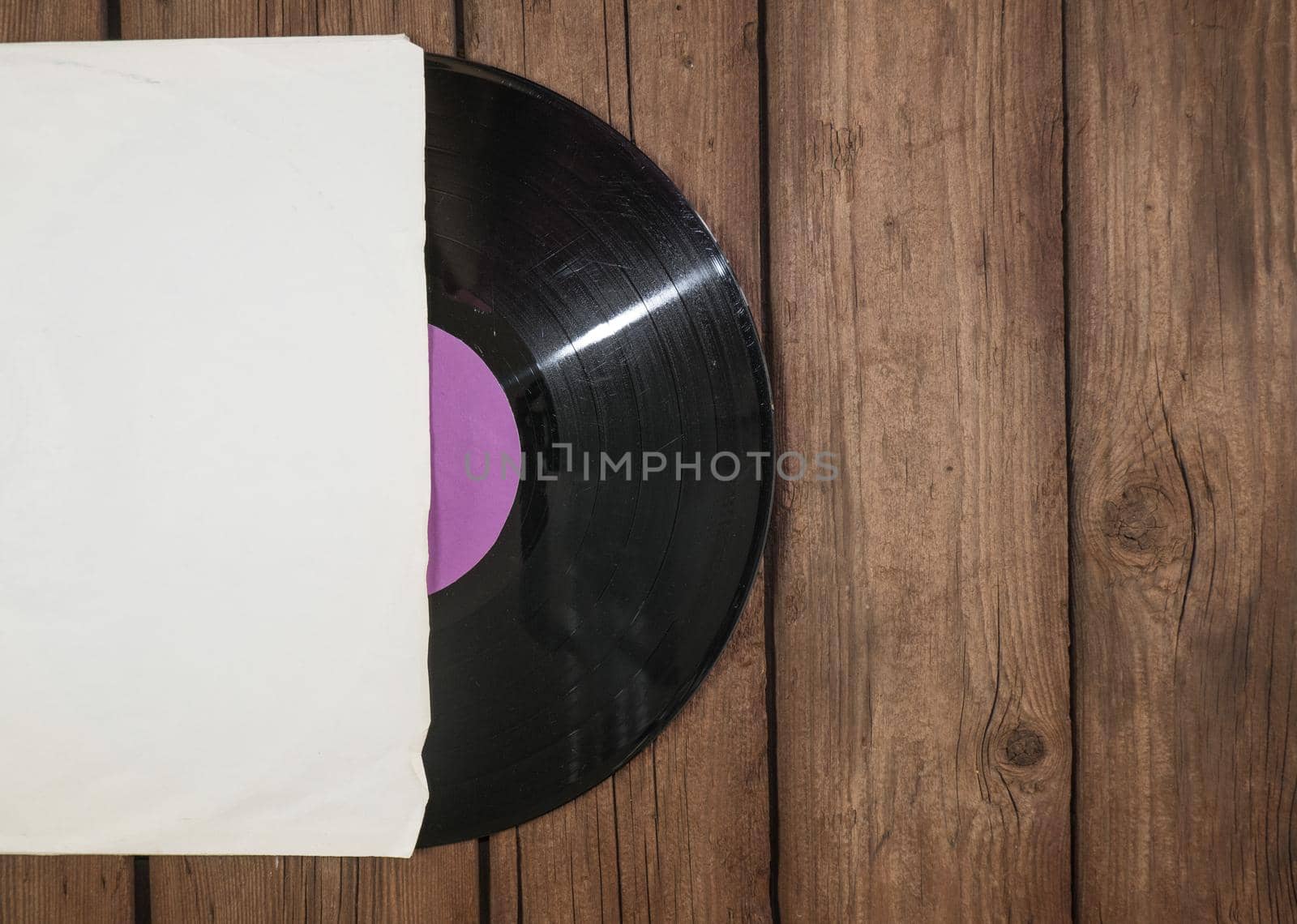 Old vinyl record in paper case on wooden rustic background.