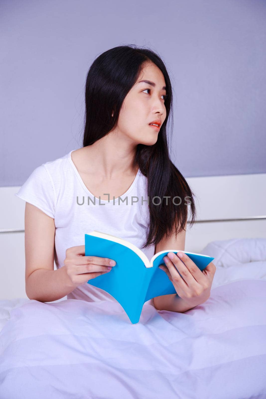 woman reading a book on bed in bedroom at home by geargodz