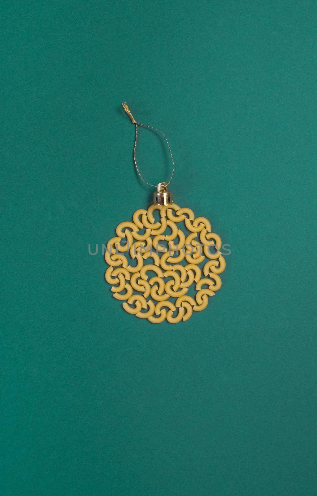 Christmas decoration on a tree in the form of a ball of pasta on a green paper background, top view. Conceptual photo