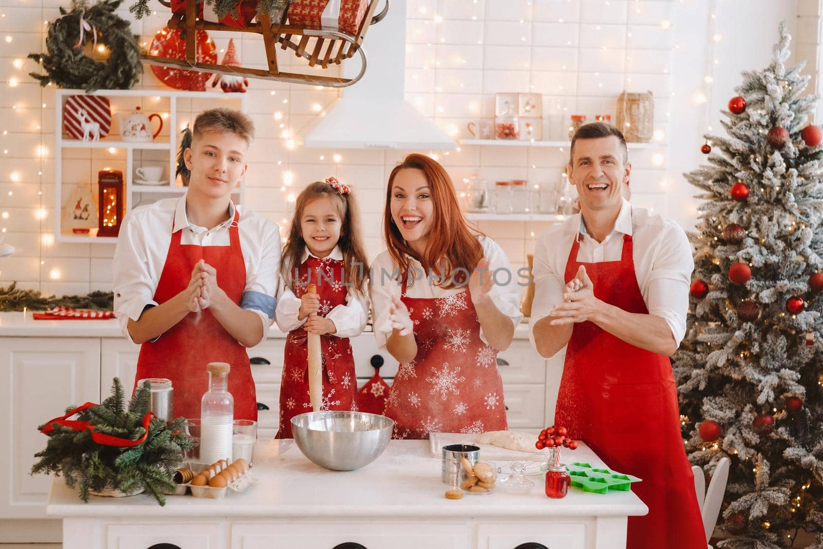 A happy family is standing in the Christmas kitchen and preparing dough for making cookies by Lobachad