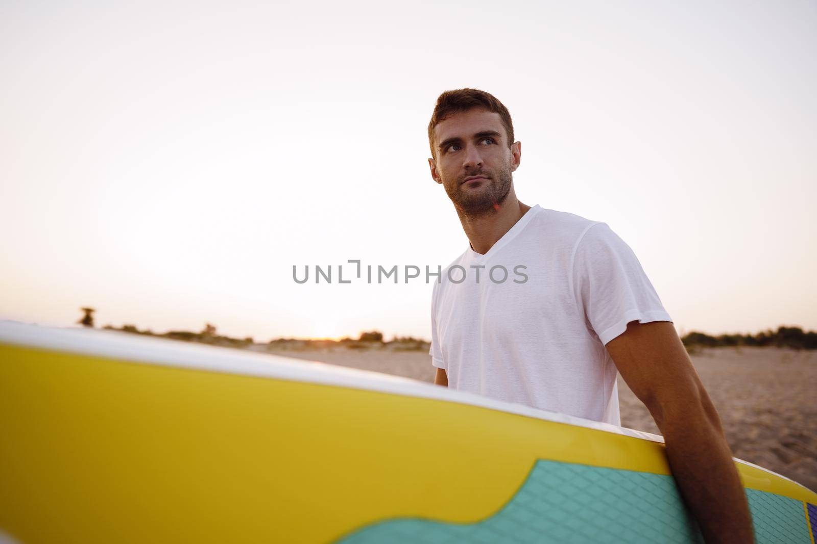 Young man carrying sup board after water surf session, close up