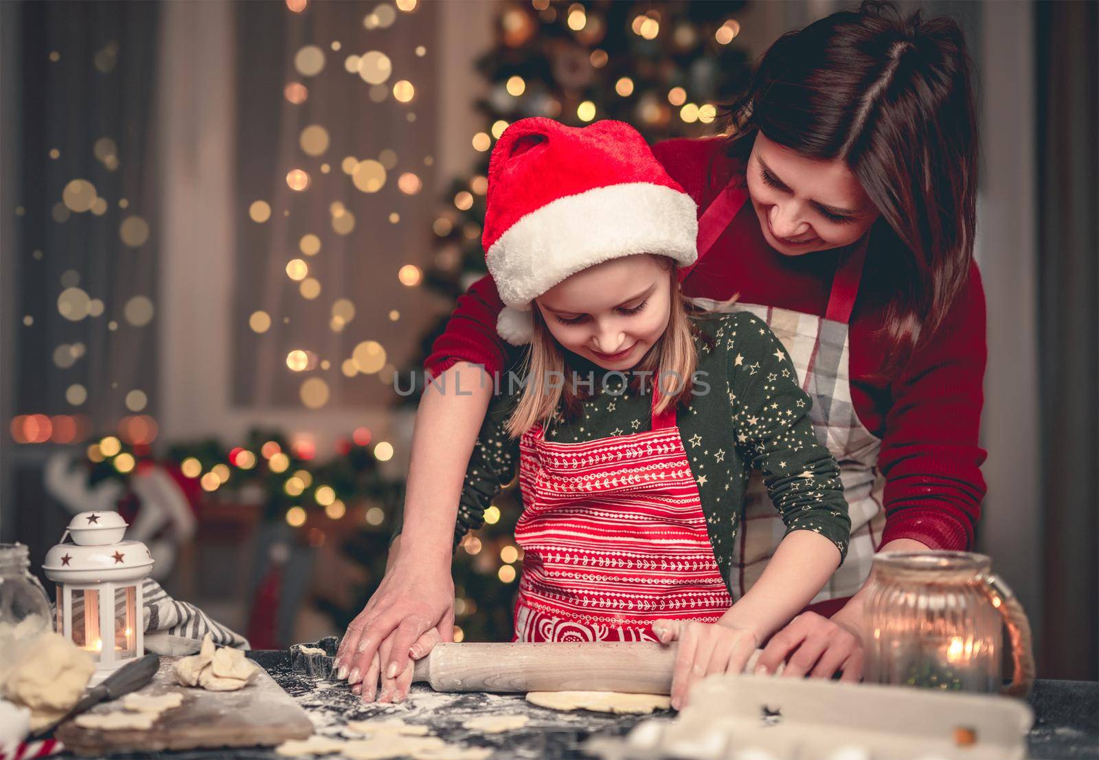 Portrait of little girl in santa hat cutting cookies on decorated christmas tree background