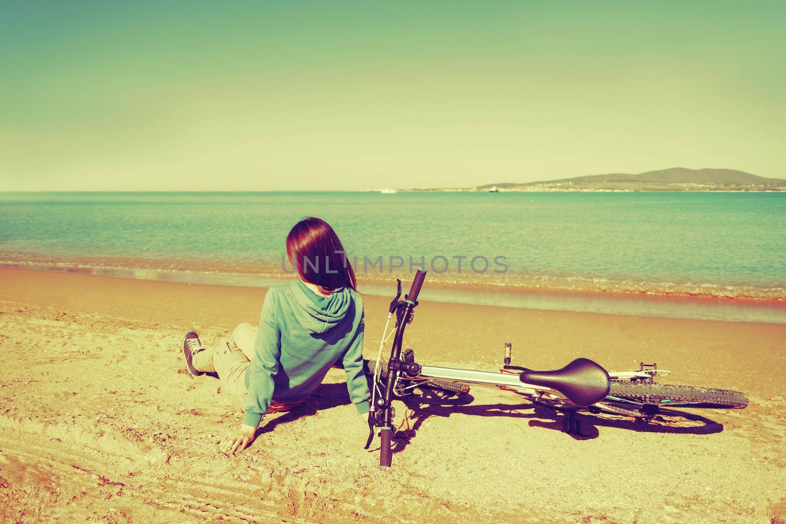 Young woman sitting near a bicycle on beach in summer. Image with instagram filter
