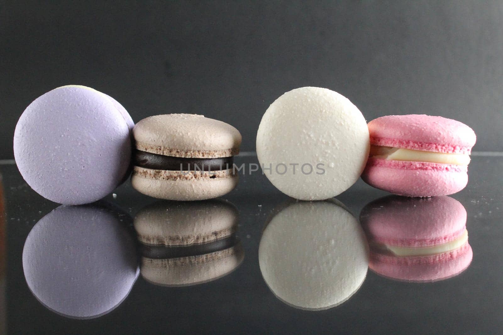 Four cakes blue purple pink coffee white macarons lie on a mirrored surface and are reflected on a black background with a place for text.