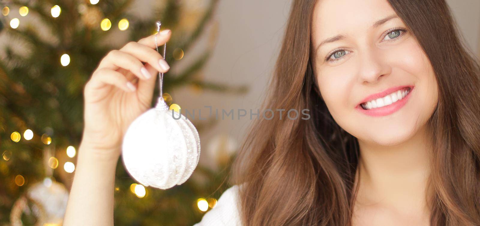 Decorating Christmas tree and winter holidays concept. Happy smiling woman holding festive ornament at home by Anneleven