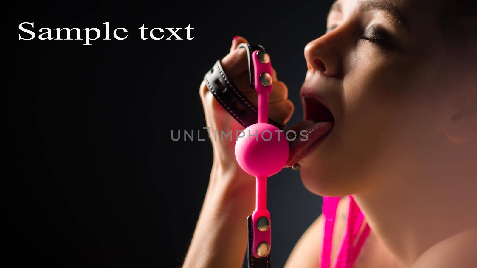 BDSM outfit for adult sex games. A young woman licks pink gag ball - image