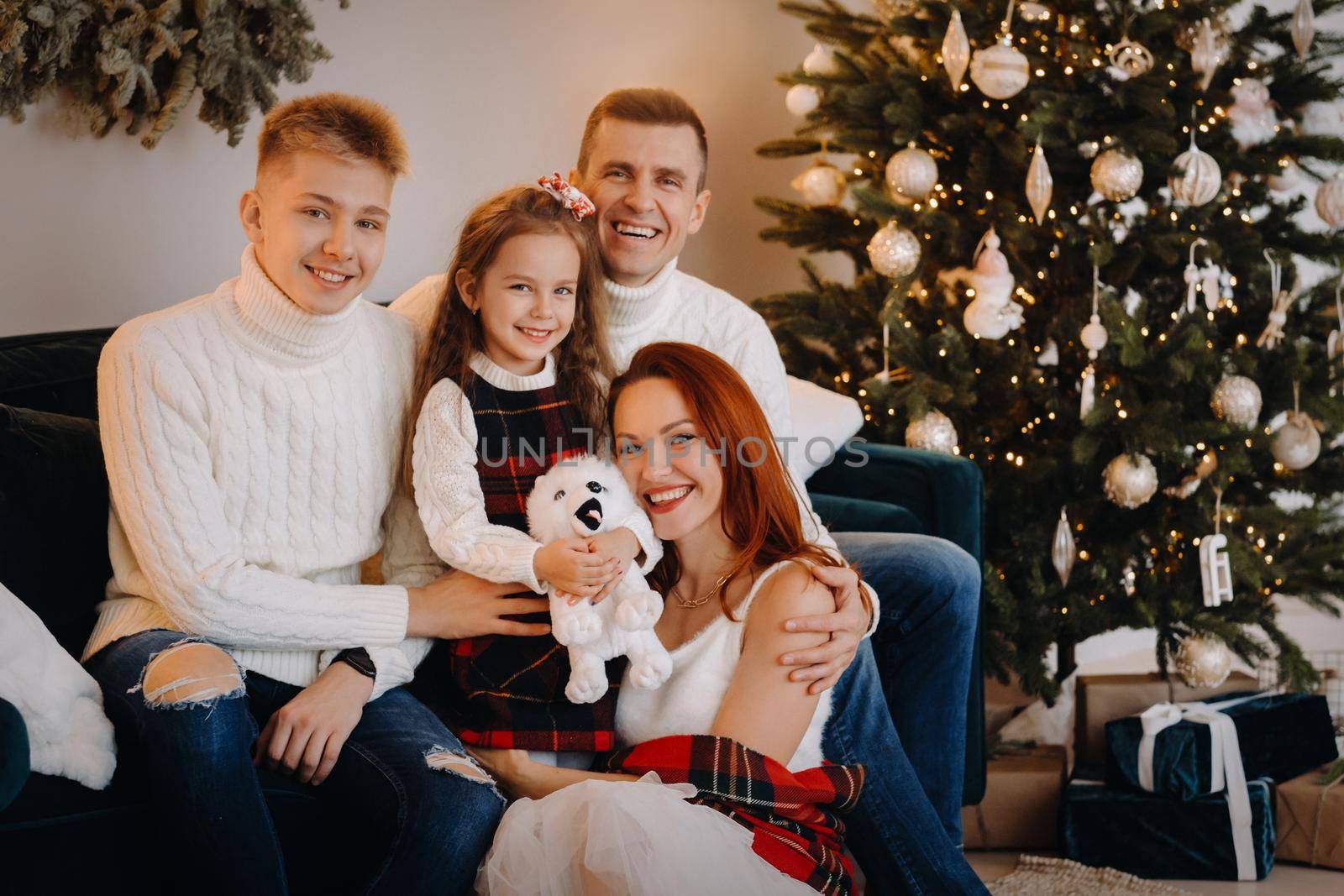 Close-up portrait of a happy family sitting on a sofa near a Christmas tree celebrating a holiday by Lobachad