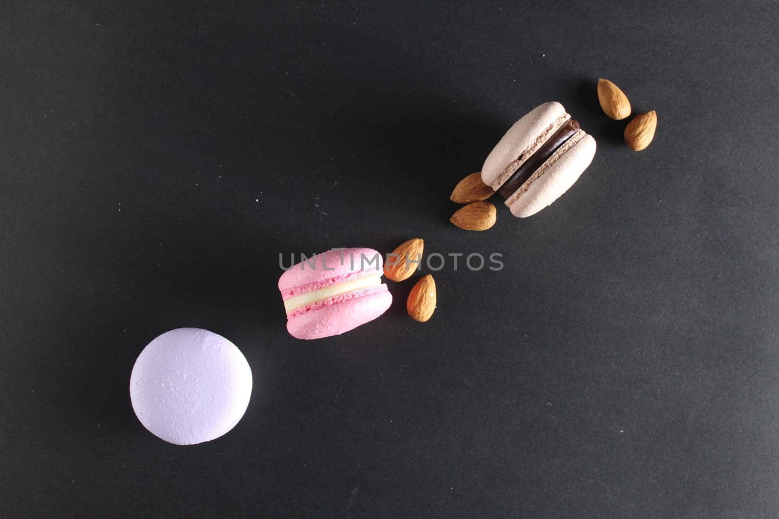 the layout top three macaroons and almond nuts lie on a black background with room for text and with a copyspace.