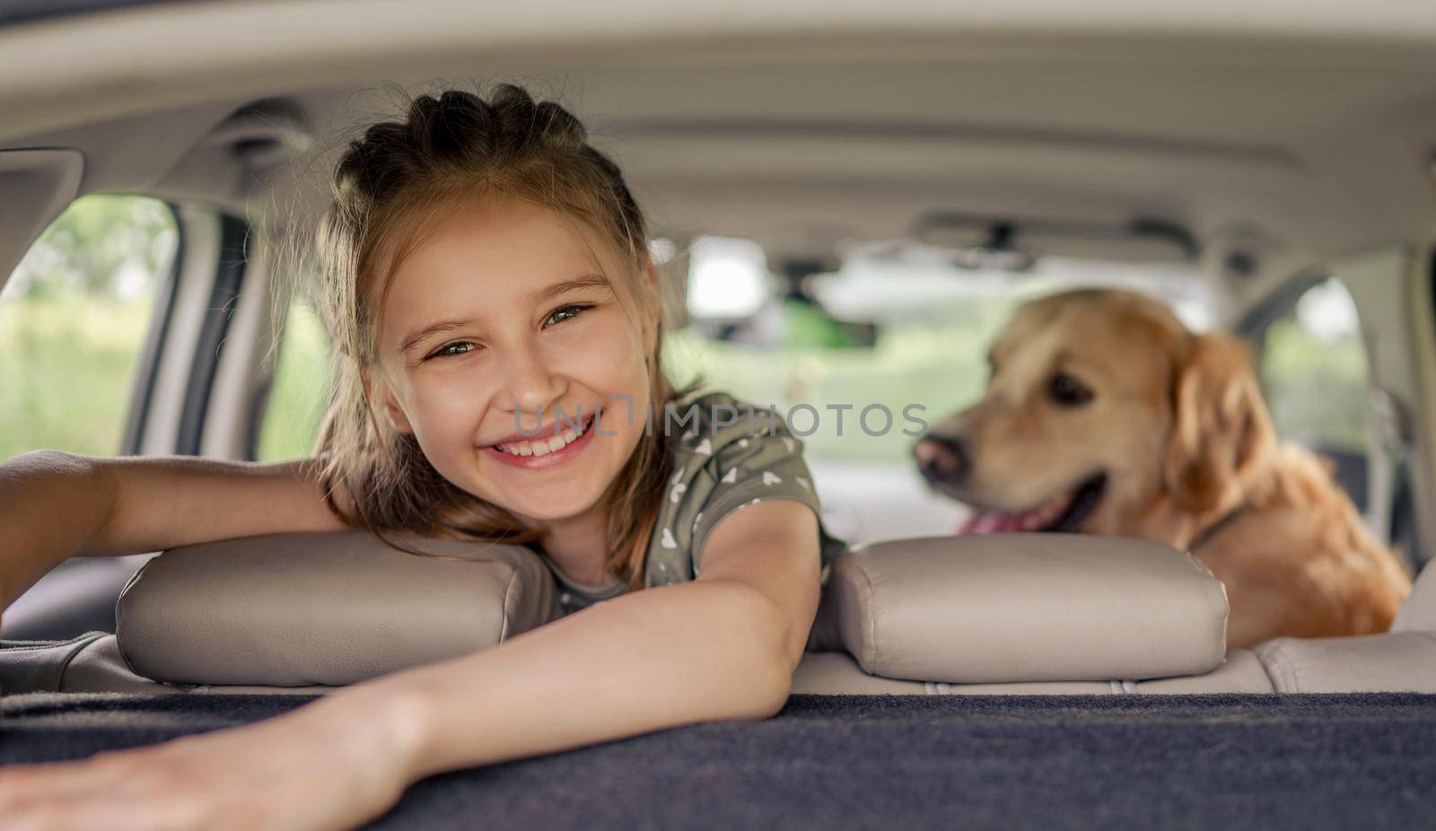 Preteen girl with golden retriever dog sitting in the car, looking at the camera and smiling. Child kid with purebred doggy pet in the vehicle inside