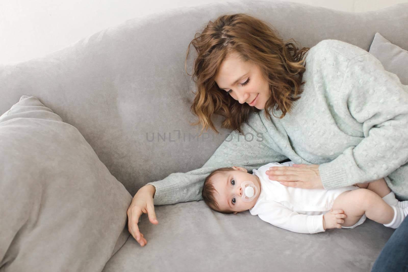 Young woman lying with cute little boy on gray sofa.