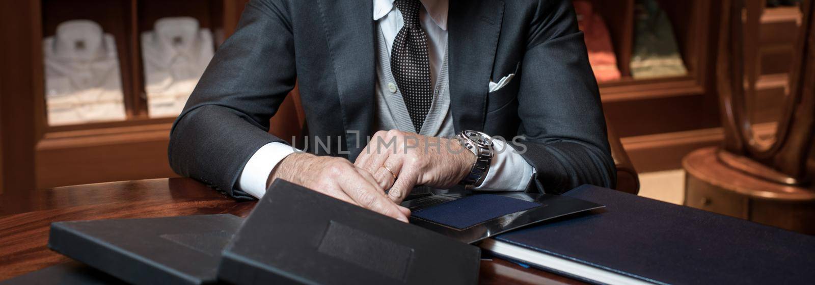Unrecognizable stylish businessman in suit sitting at table in wardrobe.