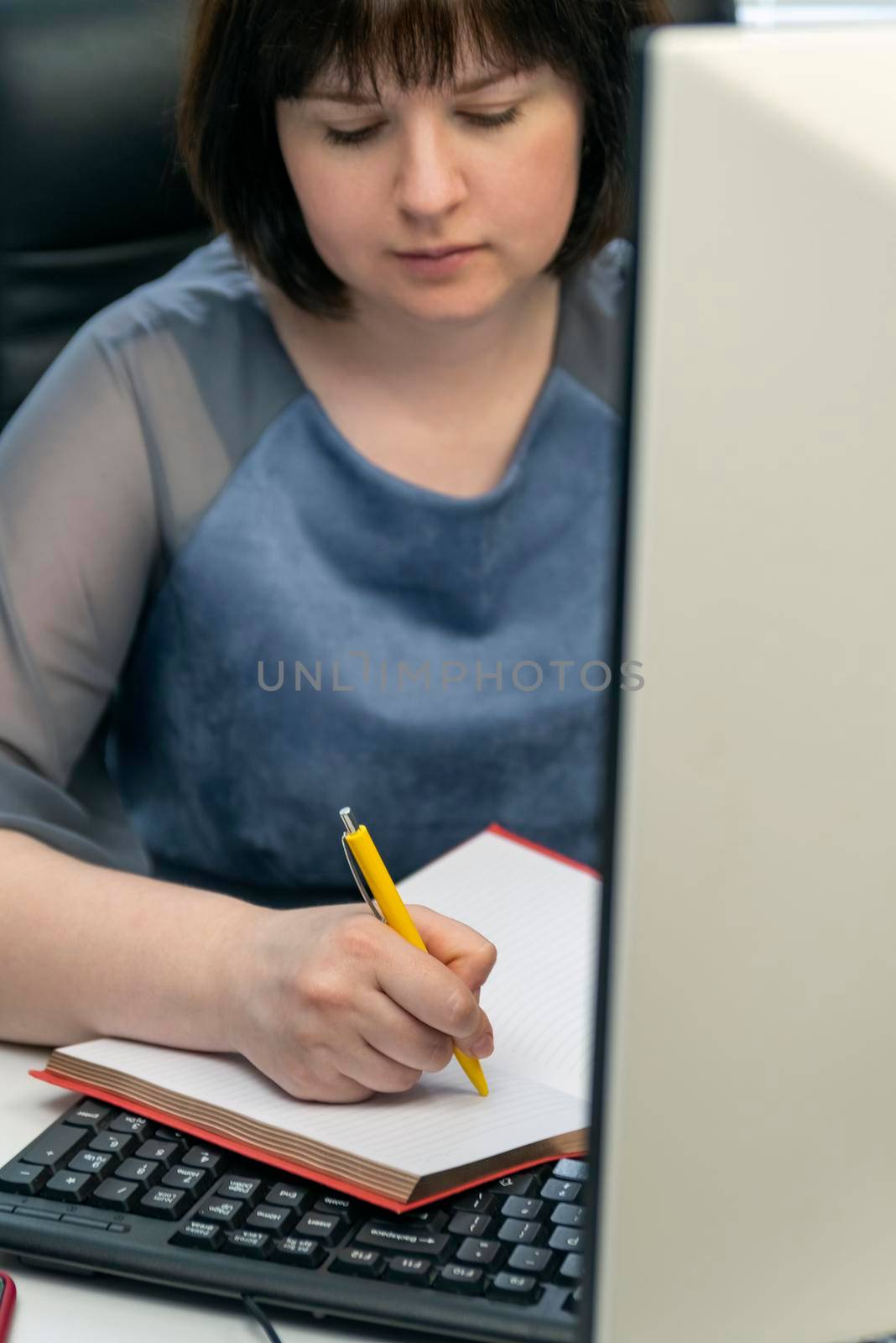 Young woman writes in notebook at workplace. Secretar at work. Task manager. Scheduling tasks