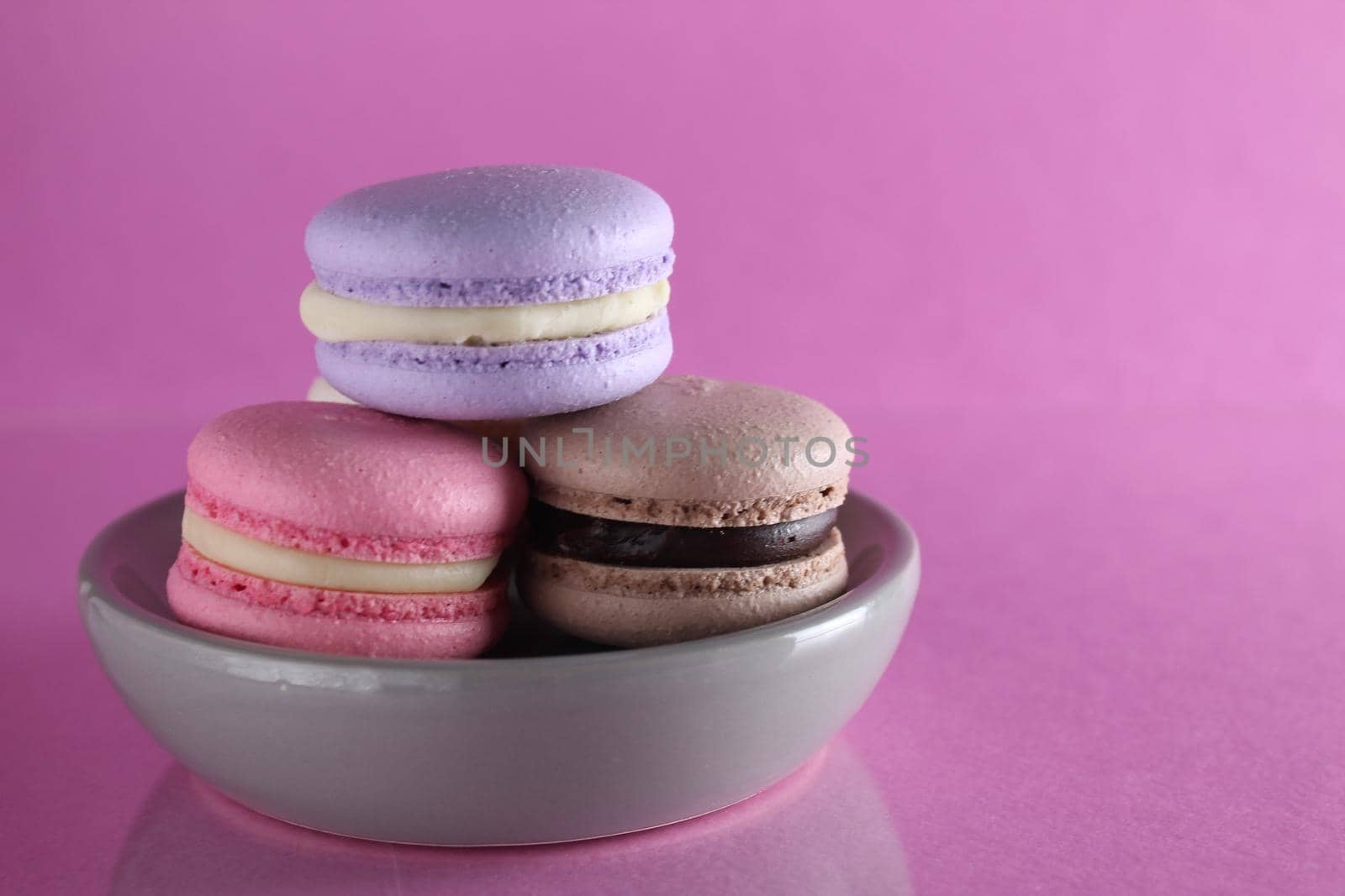 Macaroons three multicolored on a gray saucer plate stands on a pink background with a place for text and copyspace.