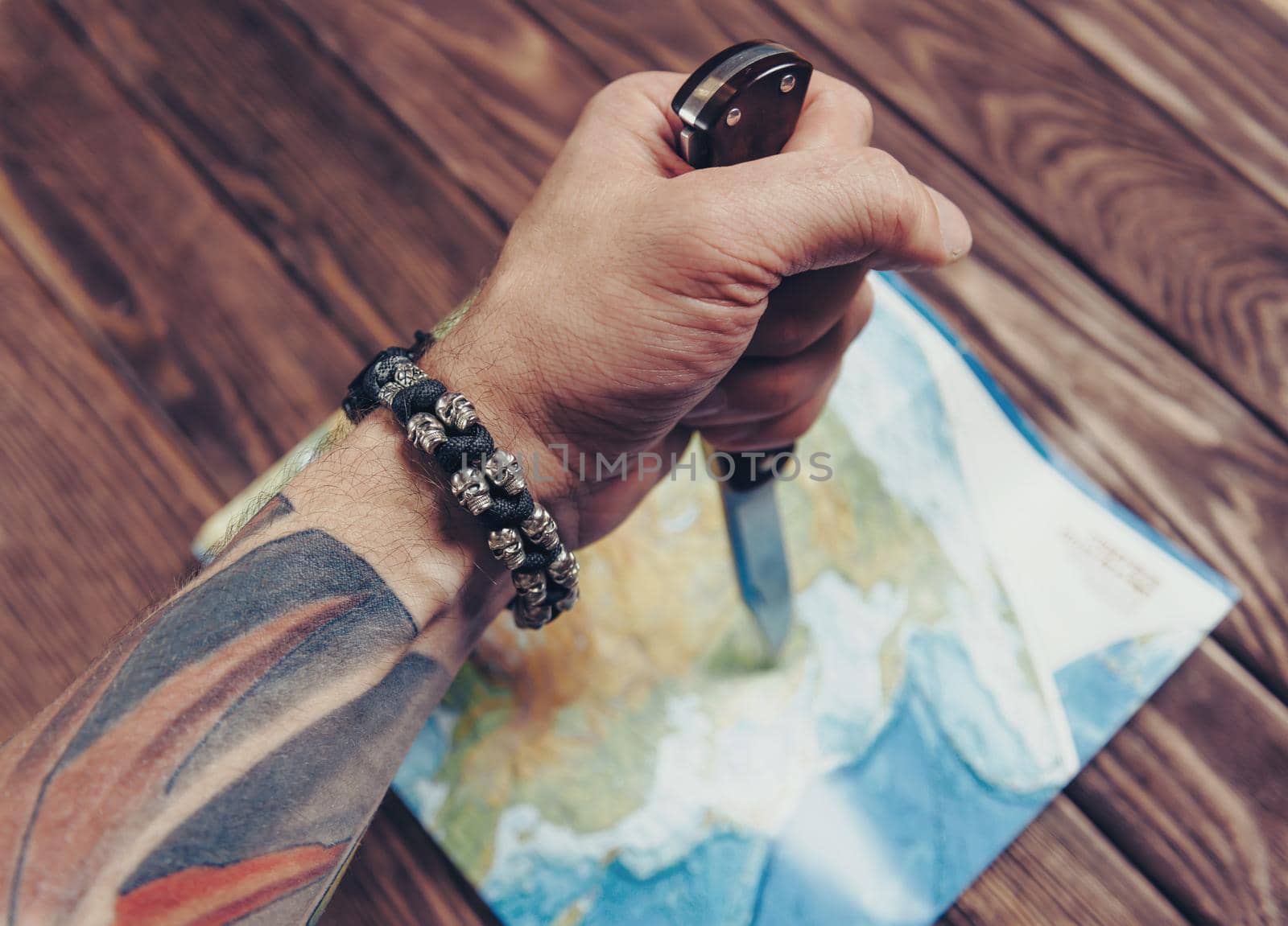 Unrecognizable man holding jackknife and pointing to map on a wooden background, view of hand.