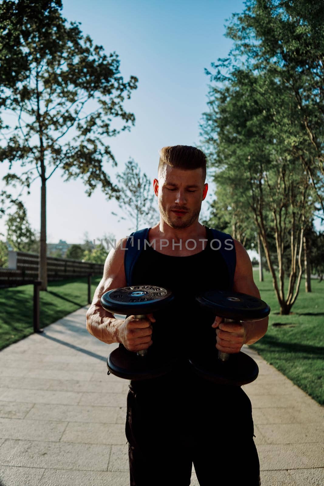 athletic man with dumbbells in his hands in the park training lifestyle. High quality photo