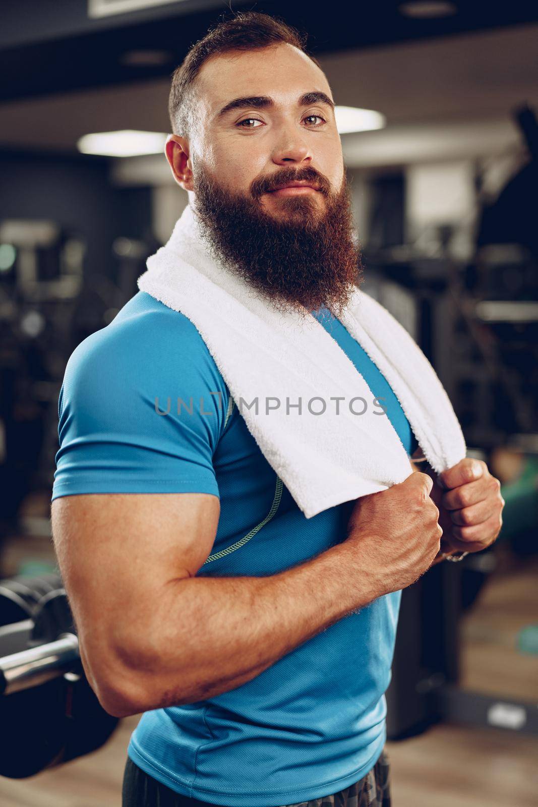 Positive bearded young man bodybuilder in blue t-shirt standing in gym