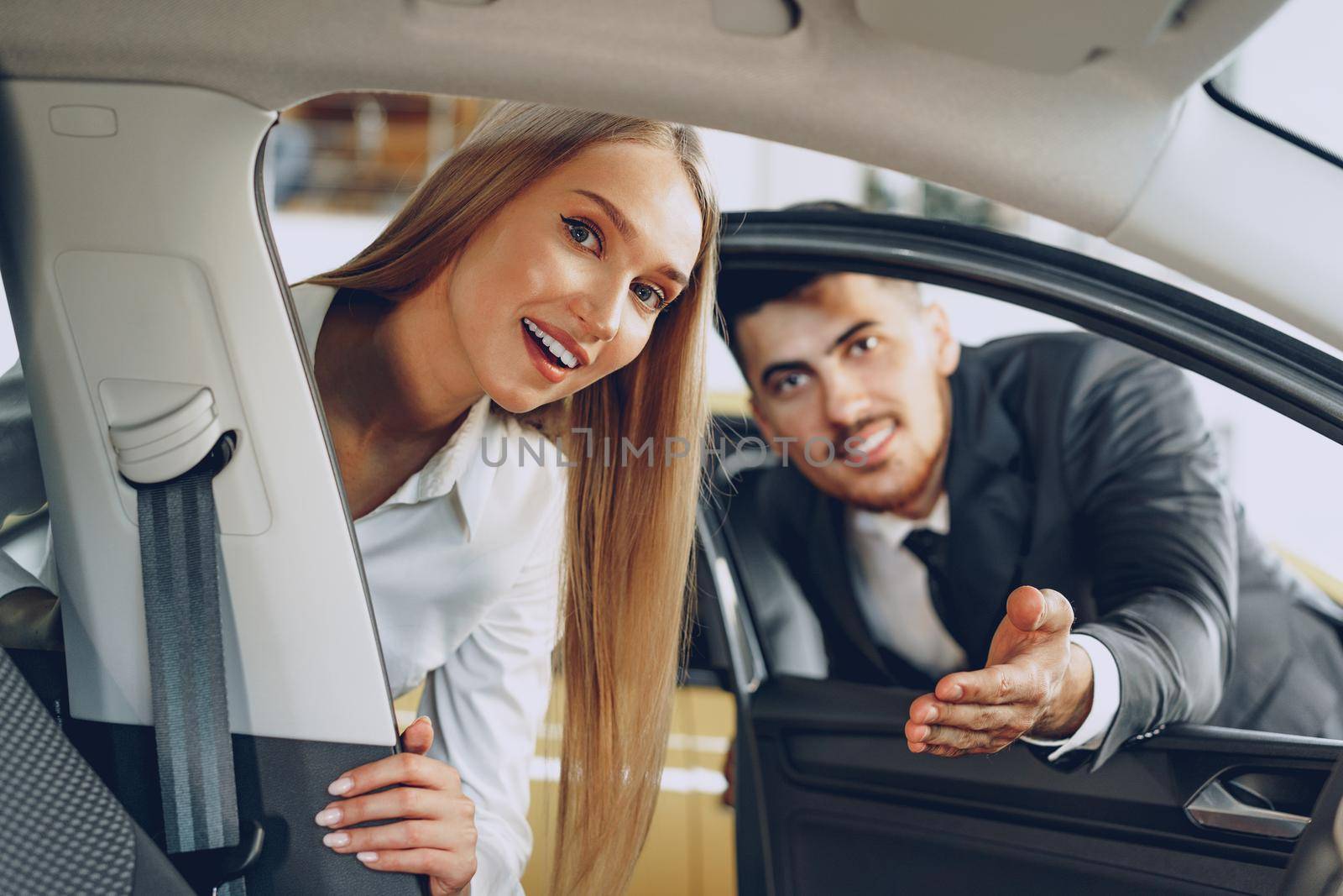 Man car dealer showing a woman buyer a new car in car salon