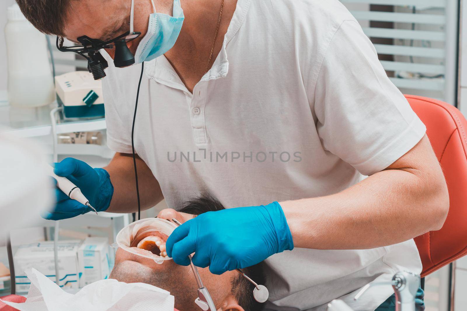 Dentist in the clinic,tartar removal procedure,the dentist in binoculars removes tartar in the patient's mouth. by Niko_Cingaryuk