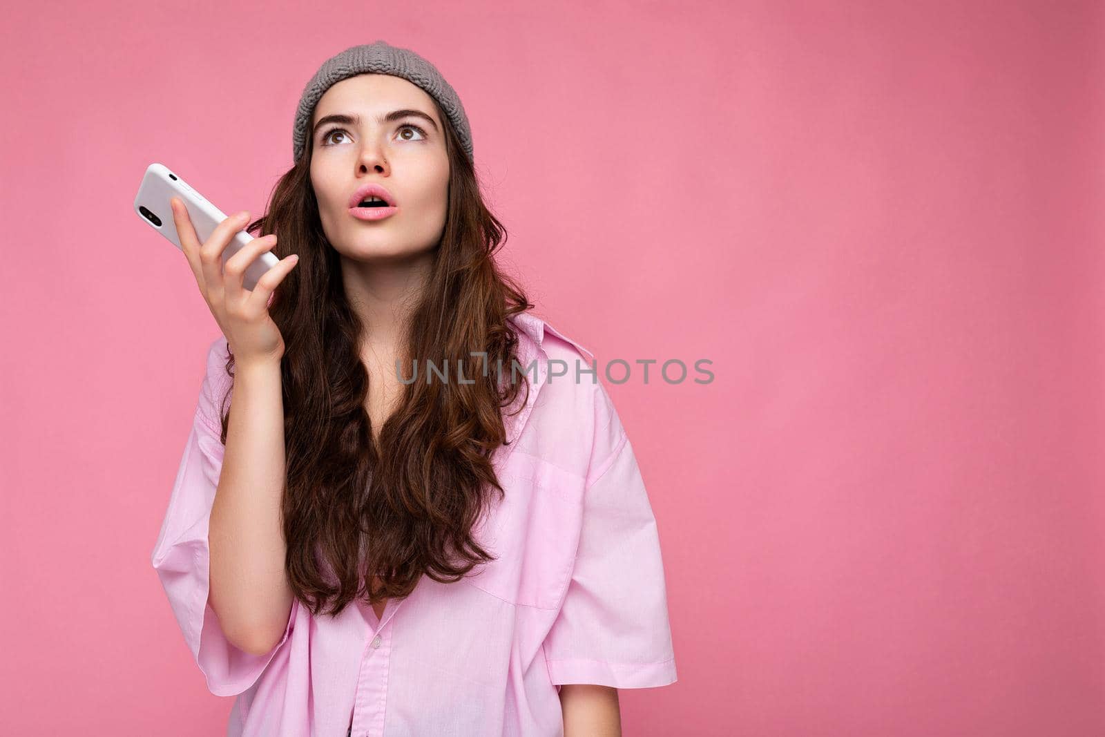Photo of attractive crazy amazed surprised young woman wearing casual stylish clothes standing isolated over background with copy space holding and using mobile phone looking up by TRMK