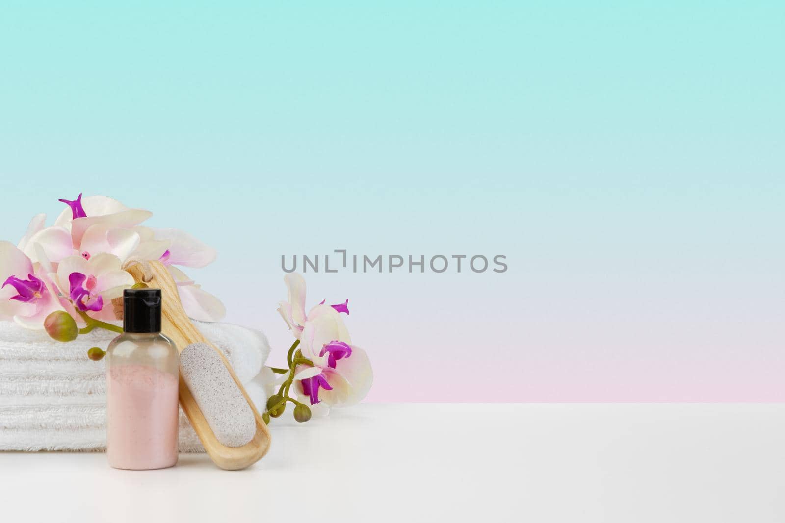 Stack of white towels and bottles of skincare on white table, front view
