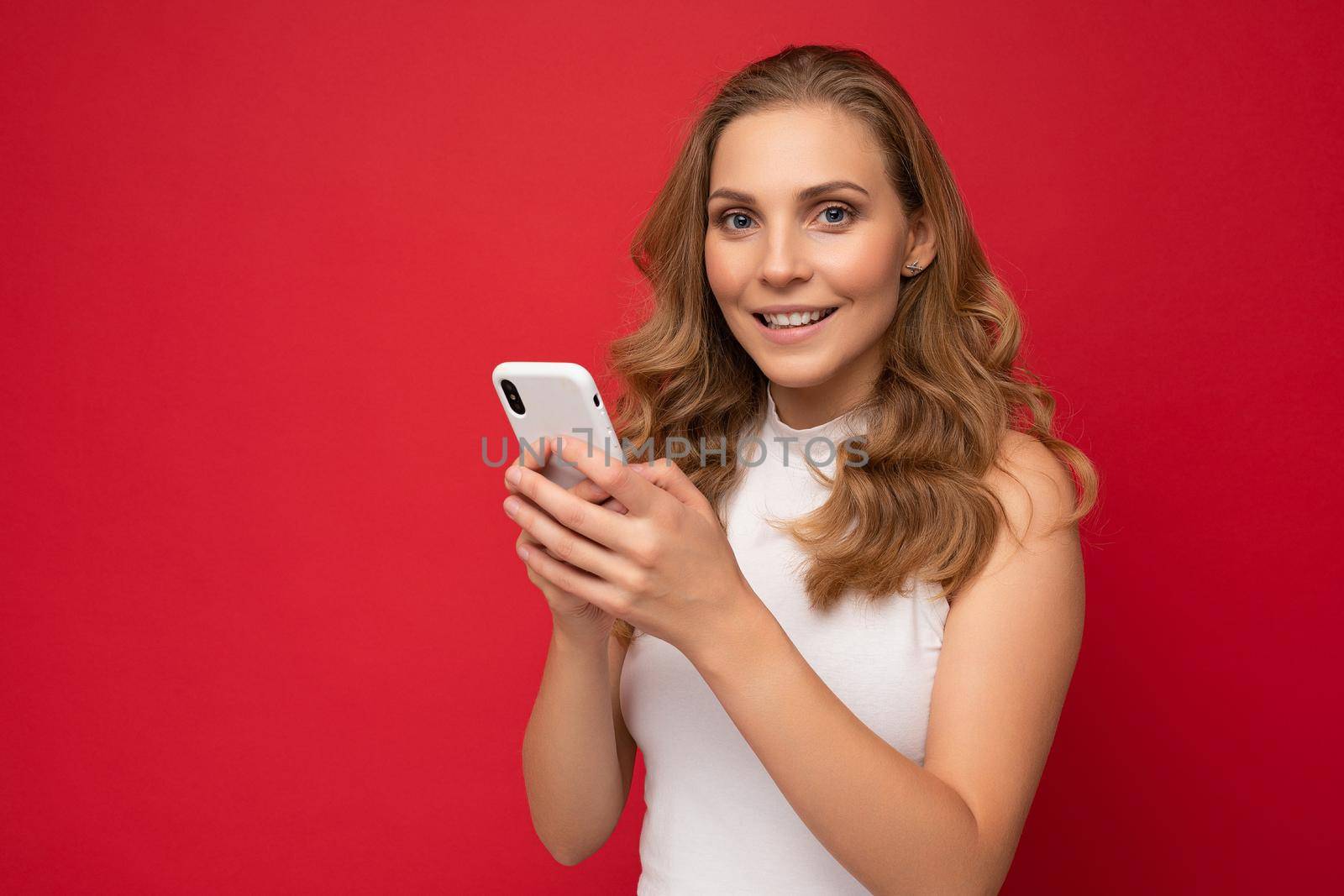 close up Photo shot of attractive positive good looking young woman wearing casual stylish outfit poising isolated on background with empty space holding in hand and using mobile phone messaging sms looking at camera.