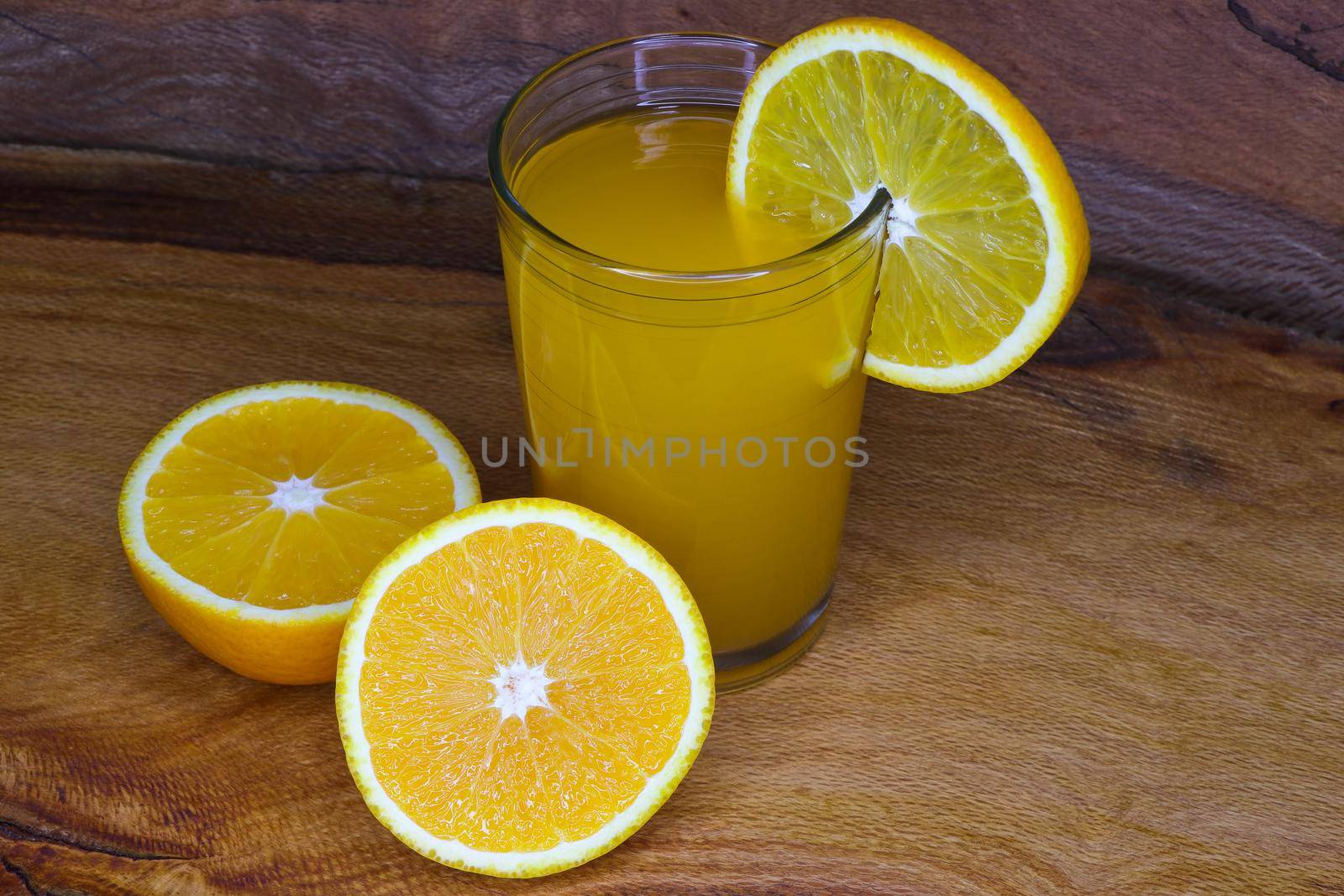 Glass of fresh orange juice with fruit slice and sliced valencia orange citrus fruit (Citrus x sinensis) on wood