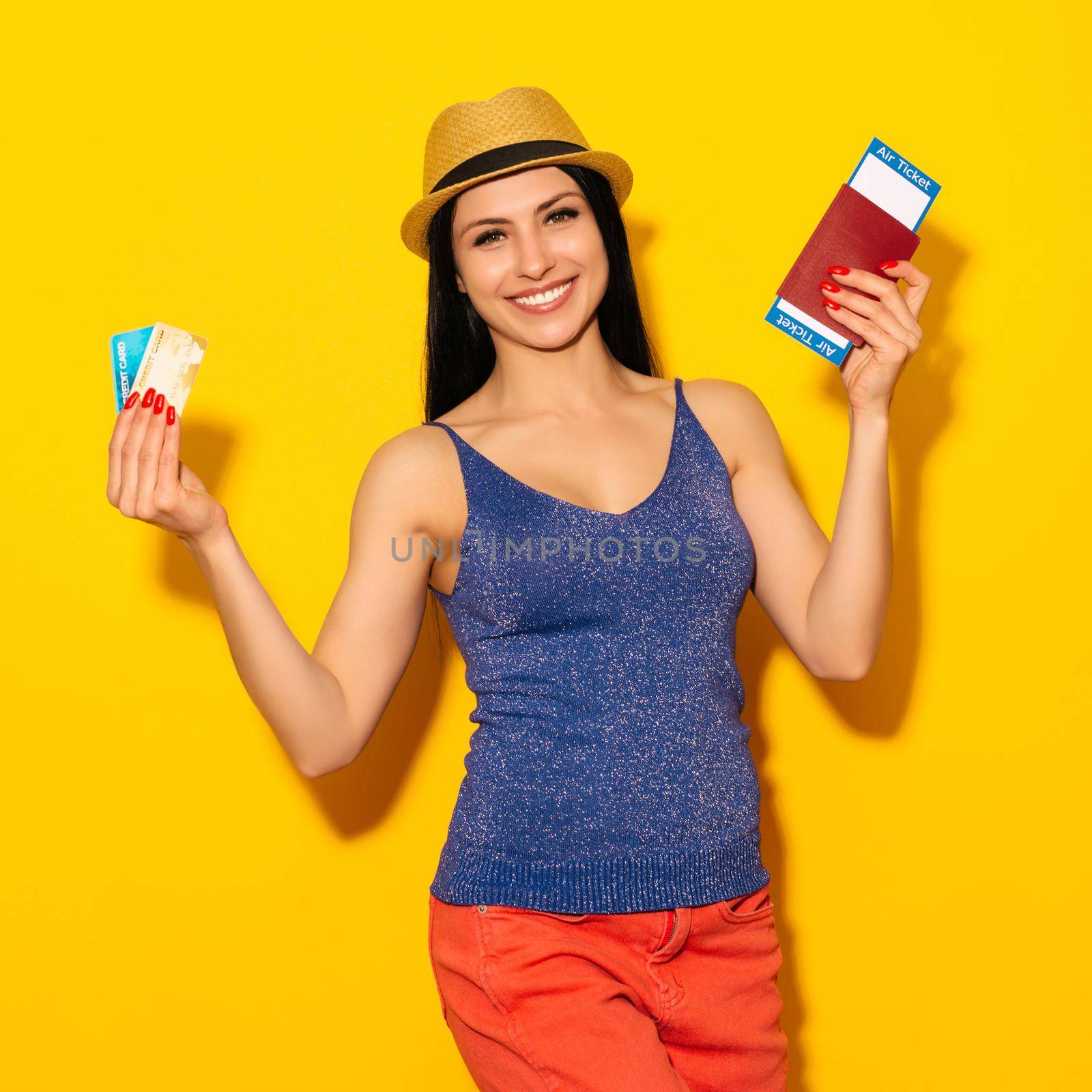 Young smiling excited woman student holding passport boarding pass ticket and credit card isolated on yellow background. Air travel flight - Image