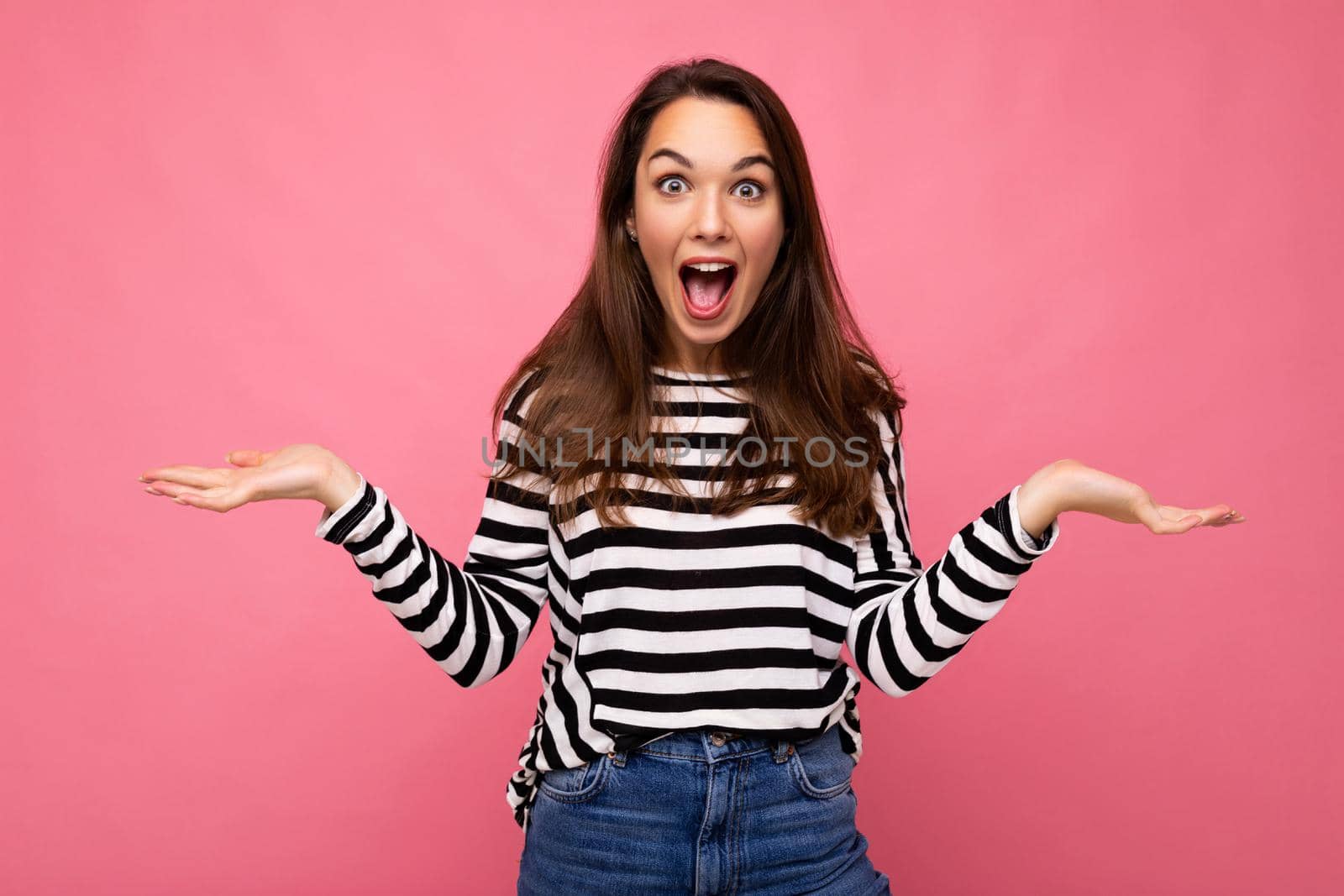 Portrait of young emotional positive happy shocked amazed attractive brunette woman with sincere emotions in casual striped pullover isolated on pink background with free space and celebrating winning shouting yes by TRMK