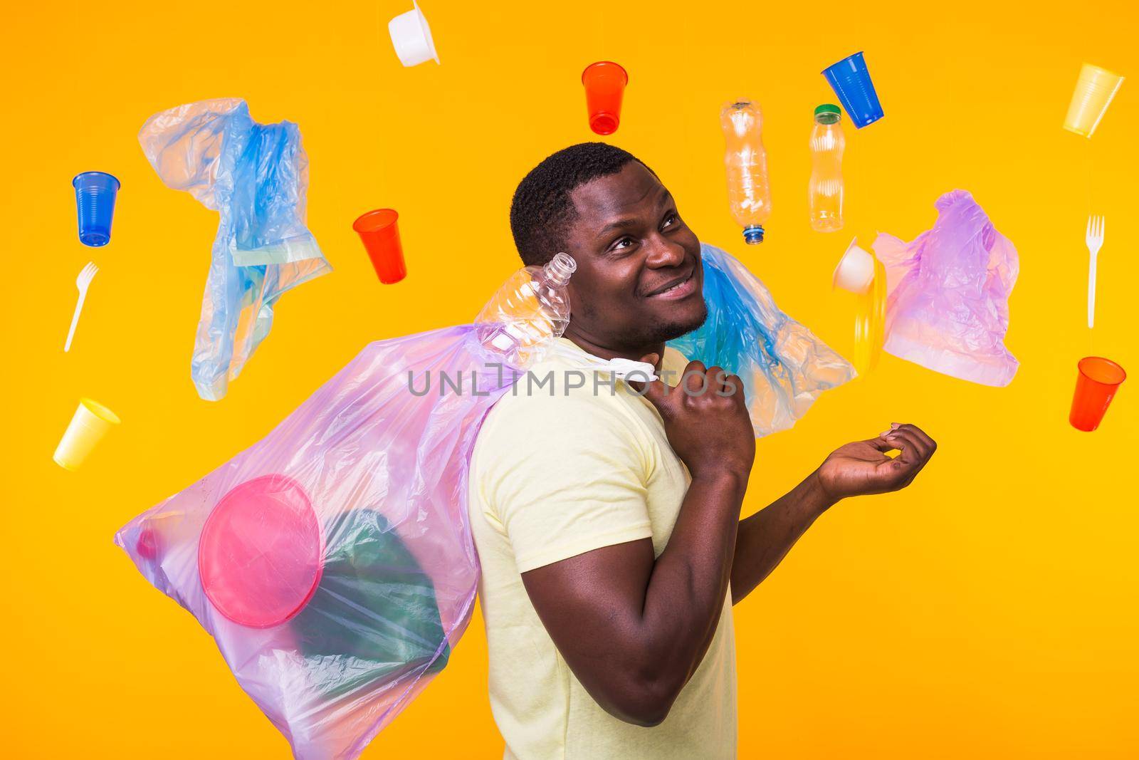Problem of trash, plastic recycling, pollution and environmental concept - confused man carrying garbage bag on yellow background.