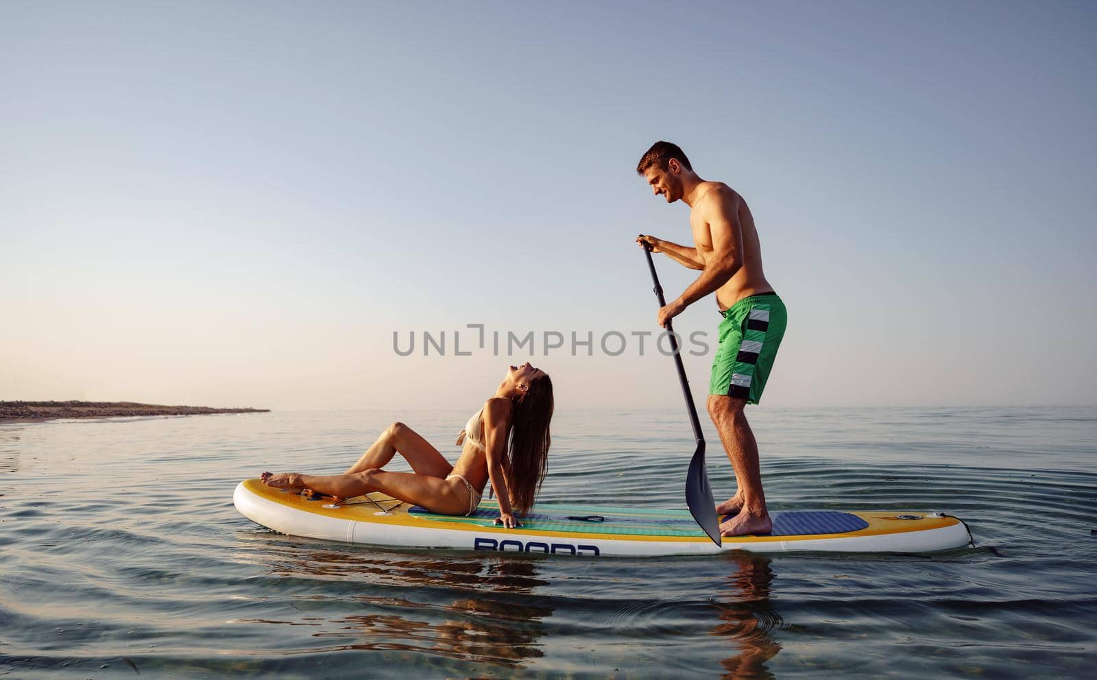 Couple of tourists young man and woman having fun paddleboarding at sea at sunset