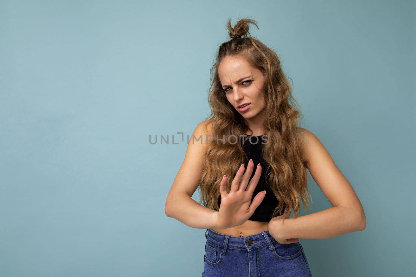 Young sad upset beautiful winsome blonde curly woman with sincere emotions wearing stylish black top isolated over blue background with copy space and showing no gesture.