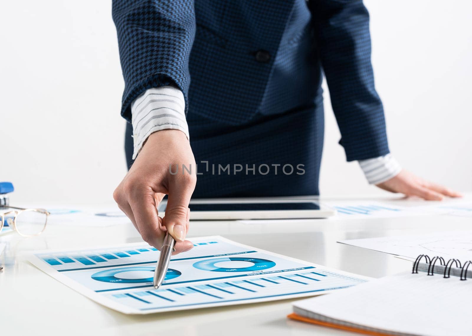 Businesswoman standing near office desk and analyzing financial charts. Successful corporate manager in business suit. Close-up woman hand with pen. Business presentation in conference room