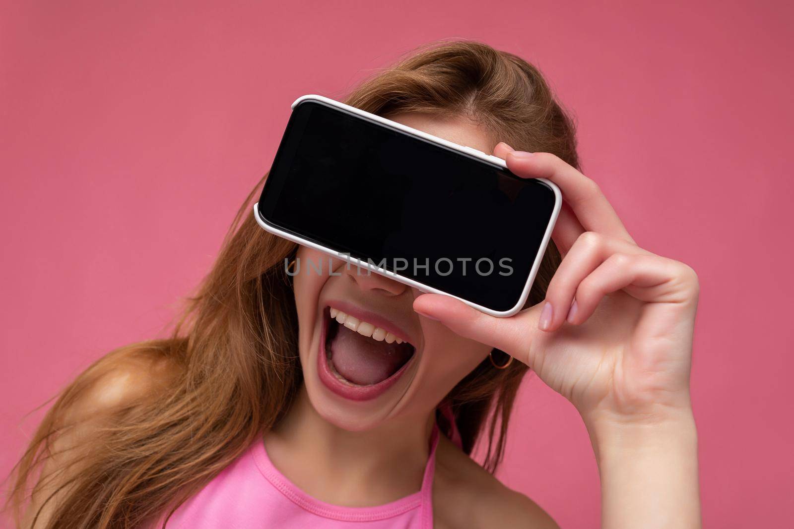 closeup Photo of overjoyed beautiful smiling young woman good looking wearing casual stylish outfit standing isolated on background with copy space holding smartphone showing phone in hand with empty screen display for mockup.