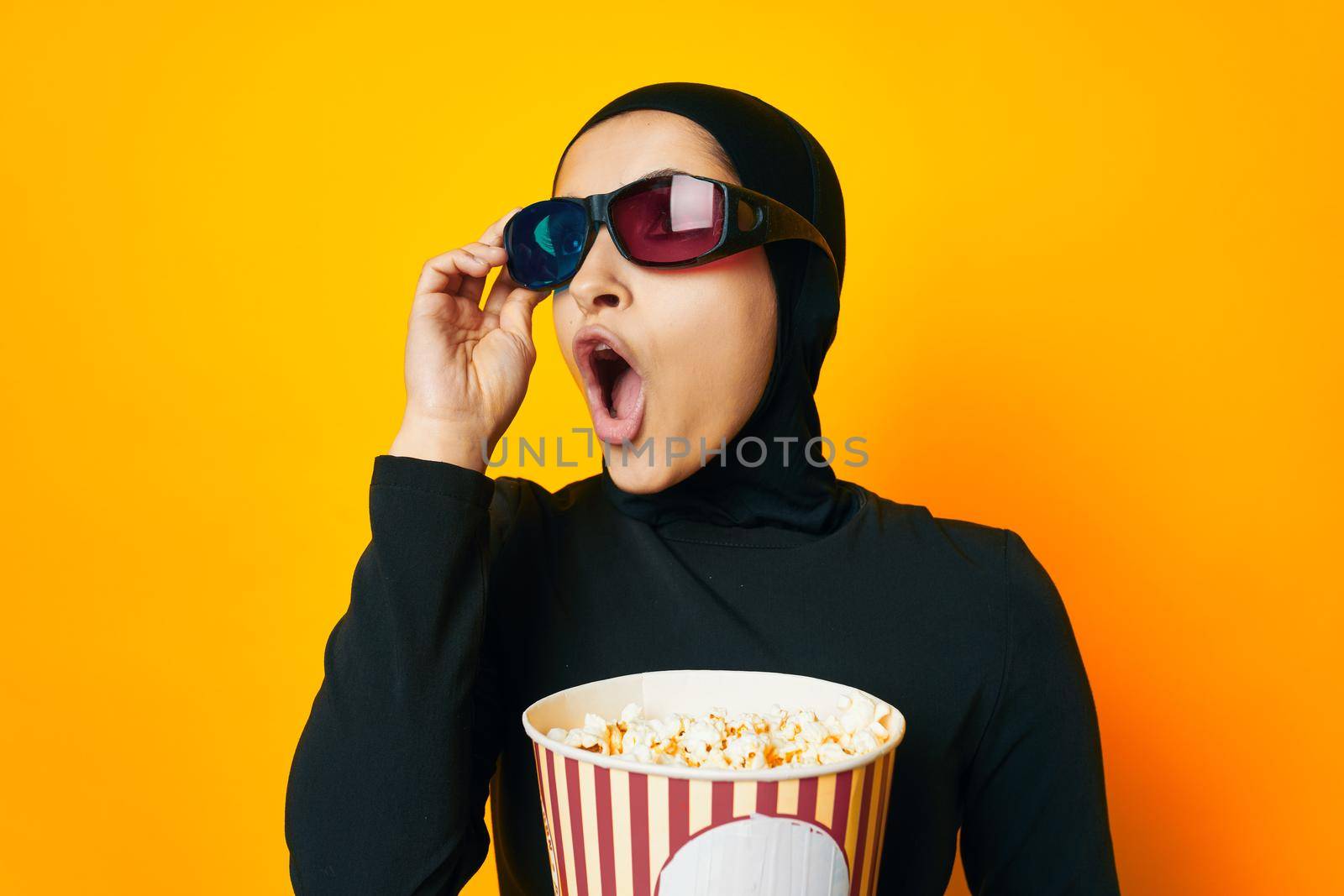 arab woman in black hijab popcorn 3D glasses cinema yellow background. High quality photo