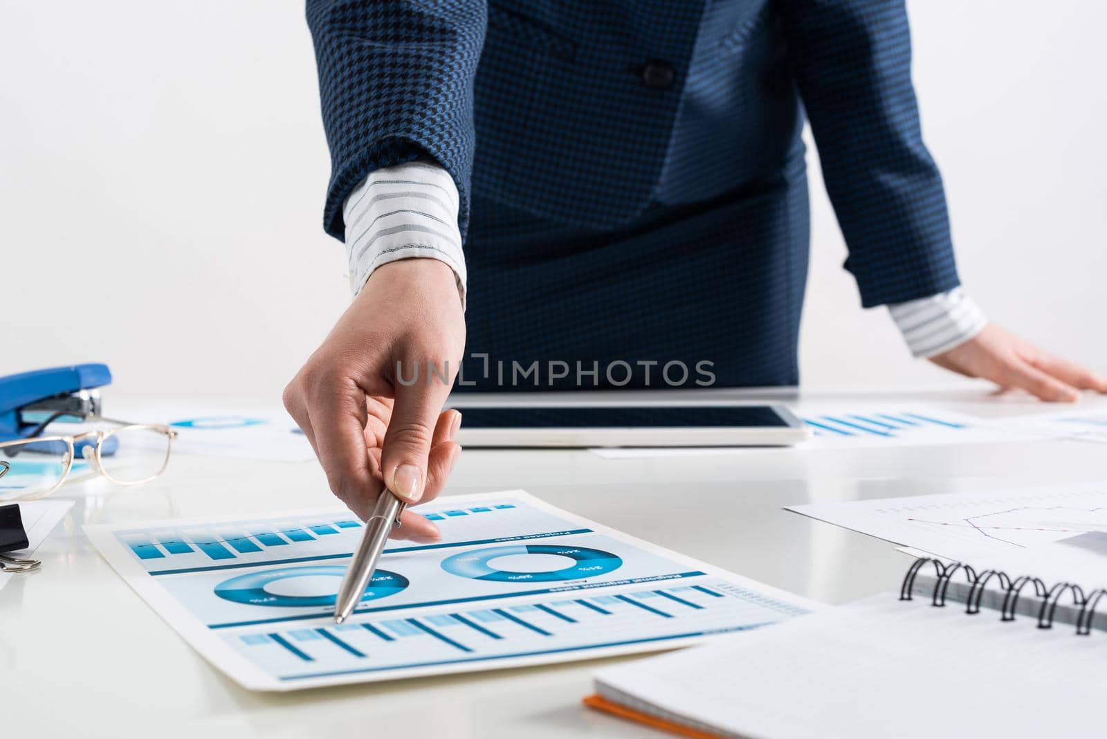 Businesswoman standing near office desk and analyzing financial charts. Successful corporate manager in business suit. Close-up woman hand with pen. Business presentation in conference room
