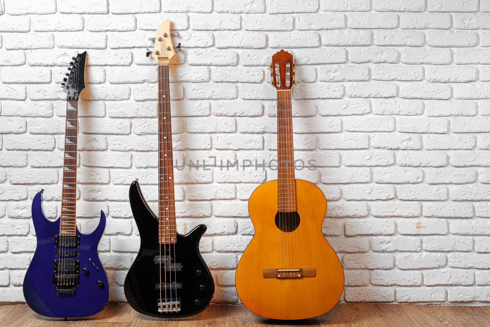 Set of guitars on the floor against white brick wall, copy space