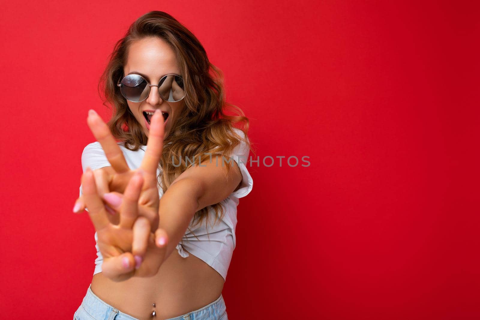 Attractive positive happy young blonde woman wearing everyday stylish clothes and modern sunglasses isolated on colorful background wall looking at camera and showing peace gesture. copy space