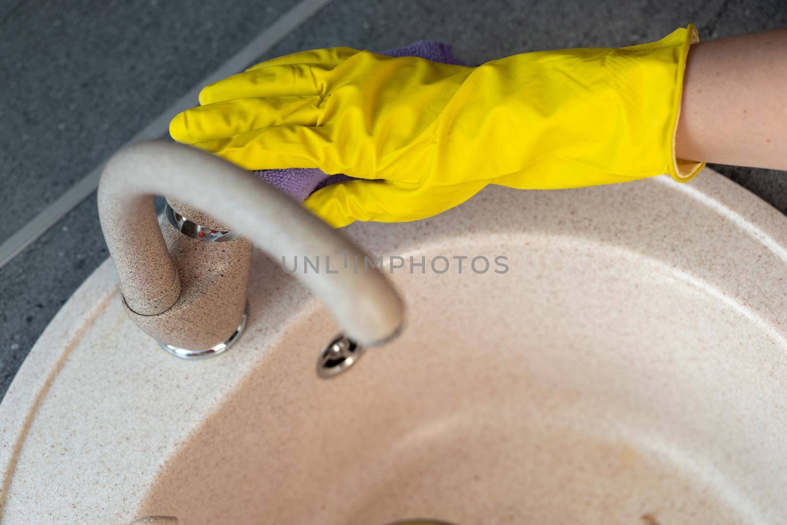 Hands in yellow gloves cleaning a sink with a sponge close up