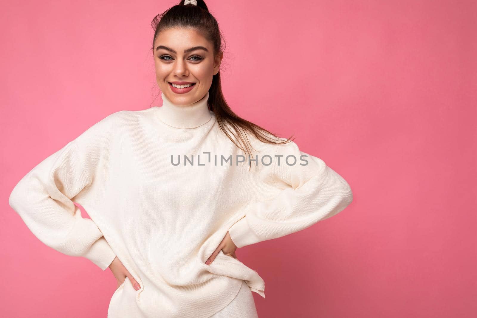 Lovely young woman wearing warm sweater standing isolated over pink background, posing.