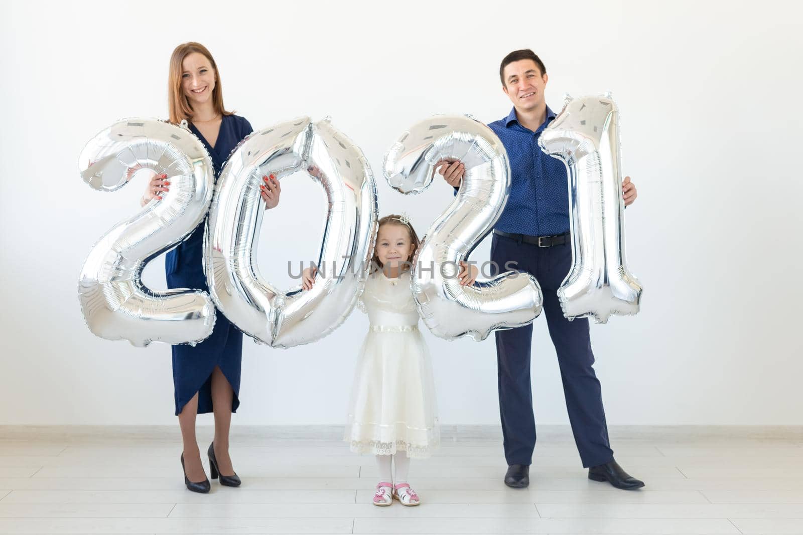 Young happy family mother and father and daughter standing near balloons shaped like numbers 2021 on white background. New year, Christmas, holiday by Satura86