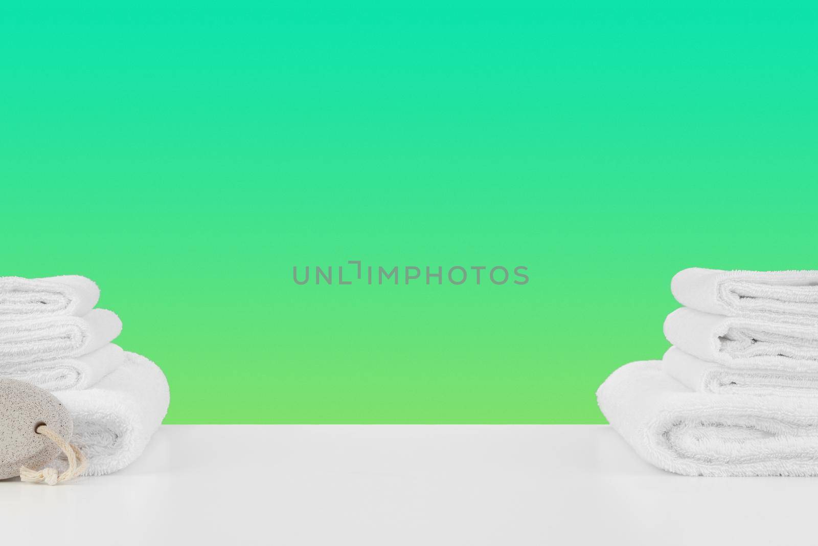 Stacked clean towels on white table against color background, front view